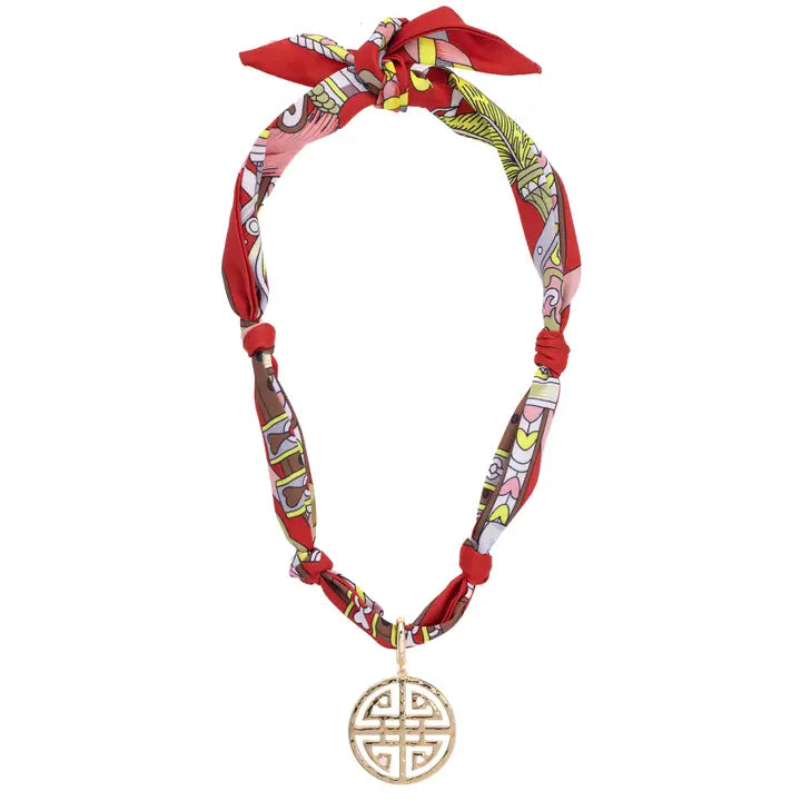 Decorative headband with red and patterned fabric, featuring a gold pendant on a white background.